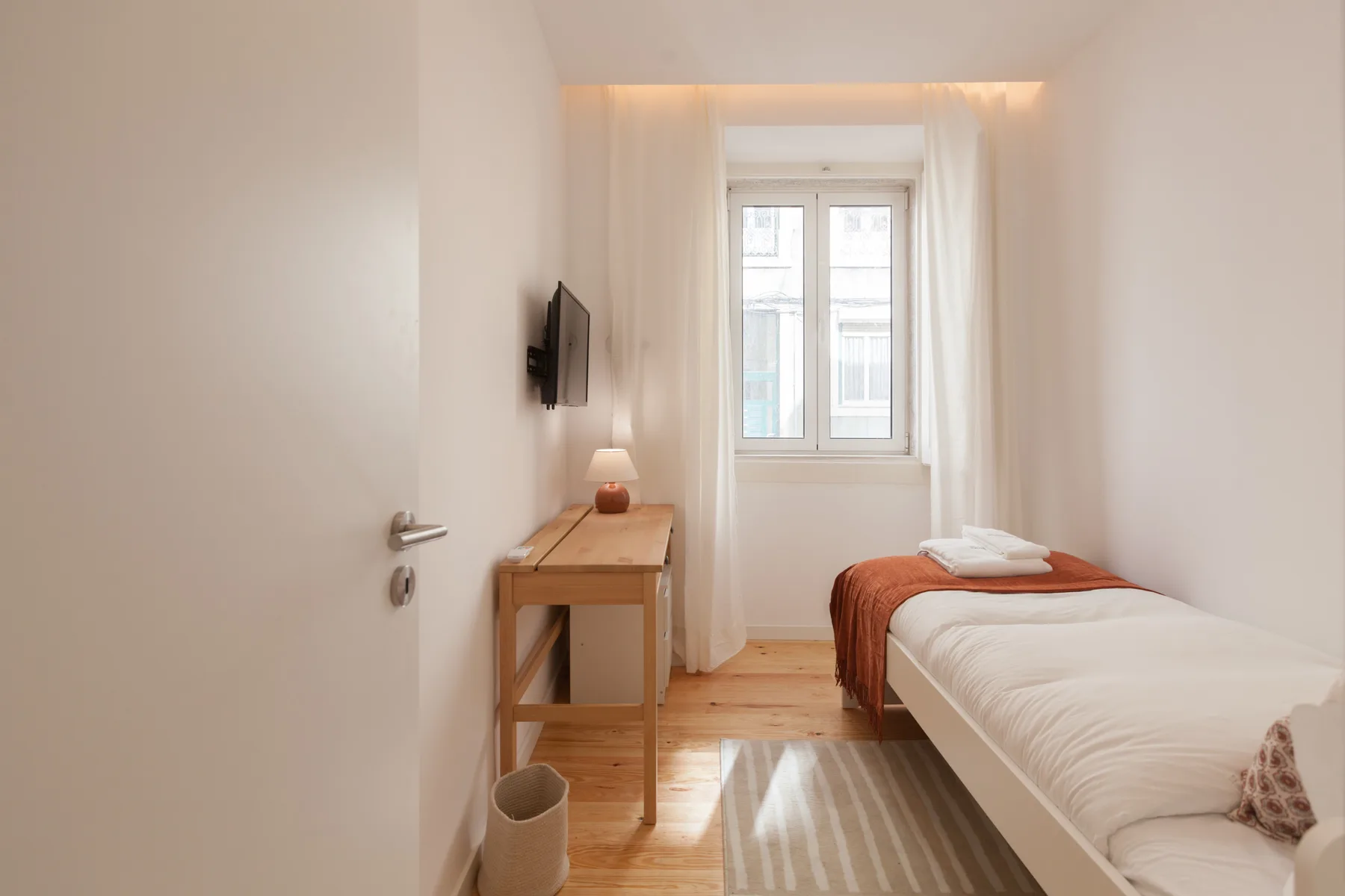 Un dormitorio luminoso con una cama individual, un escritorio y una ventana.