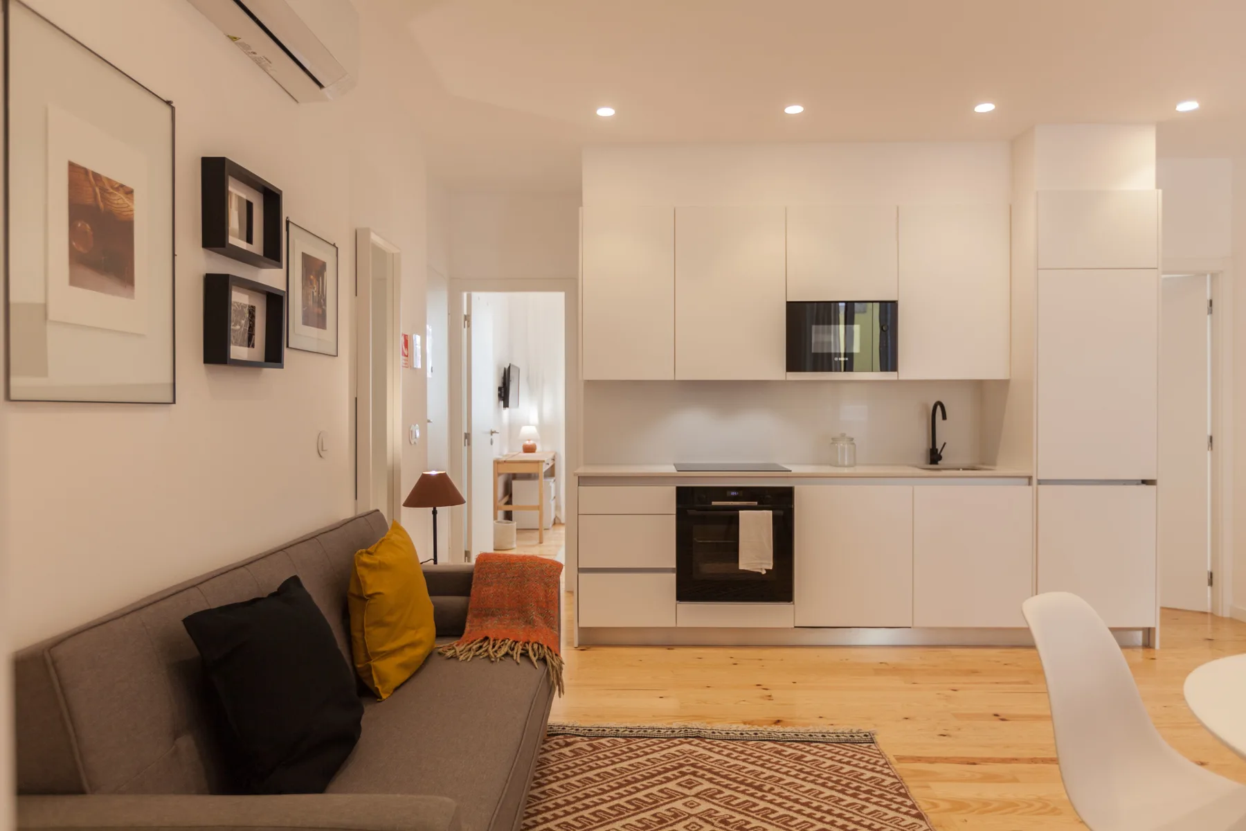 A living area opens onto a bright kitchen with white cabinetry and a dining table.