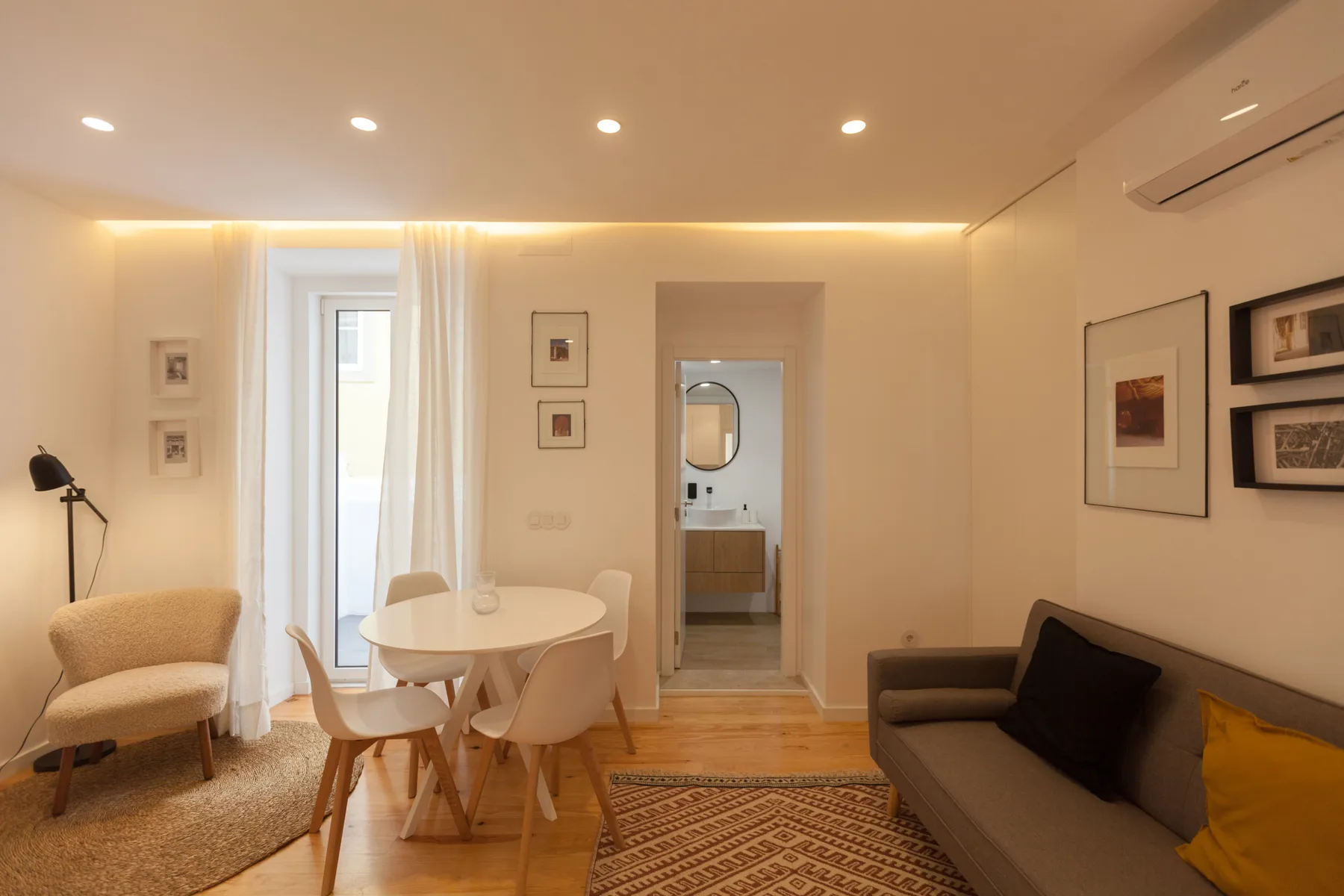 Una zona de estar y comedor con asientos alrededor de una mesa pequeña y una puerta hacia el baño.