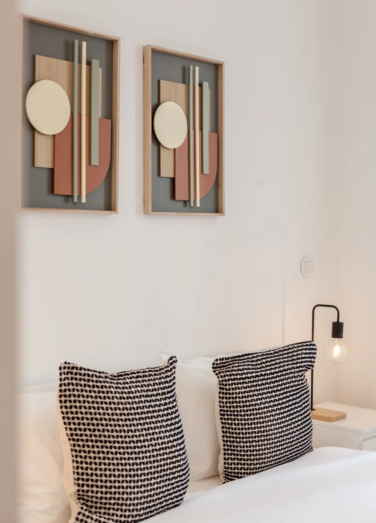 Un dormitorio con una cama bien tendida y dos cuadros abstractos enmarcados.