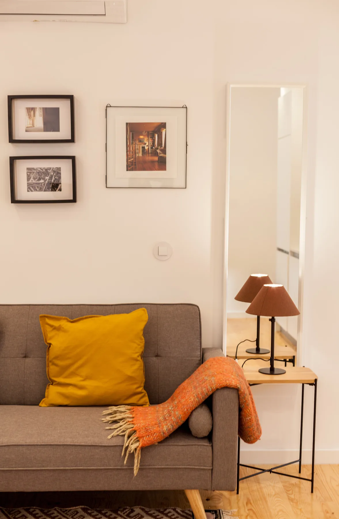 Una sala de estar con sofá, cojín amarillo y cuadros en la pared.