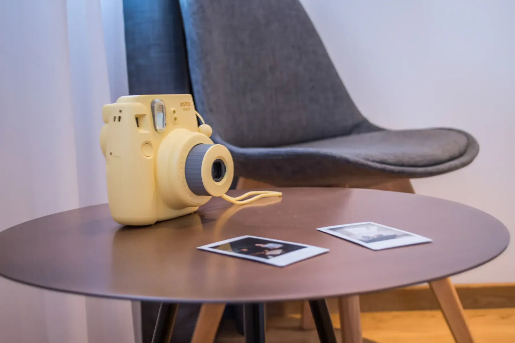 A yellow instant camera and photographs sit on a table beside a chair.