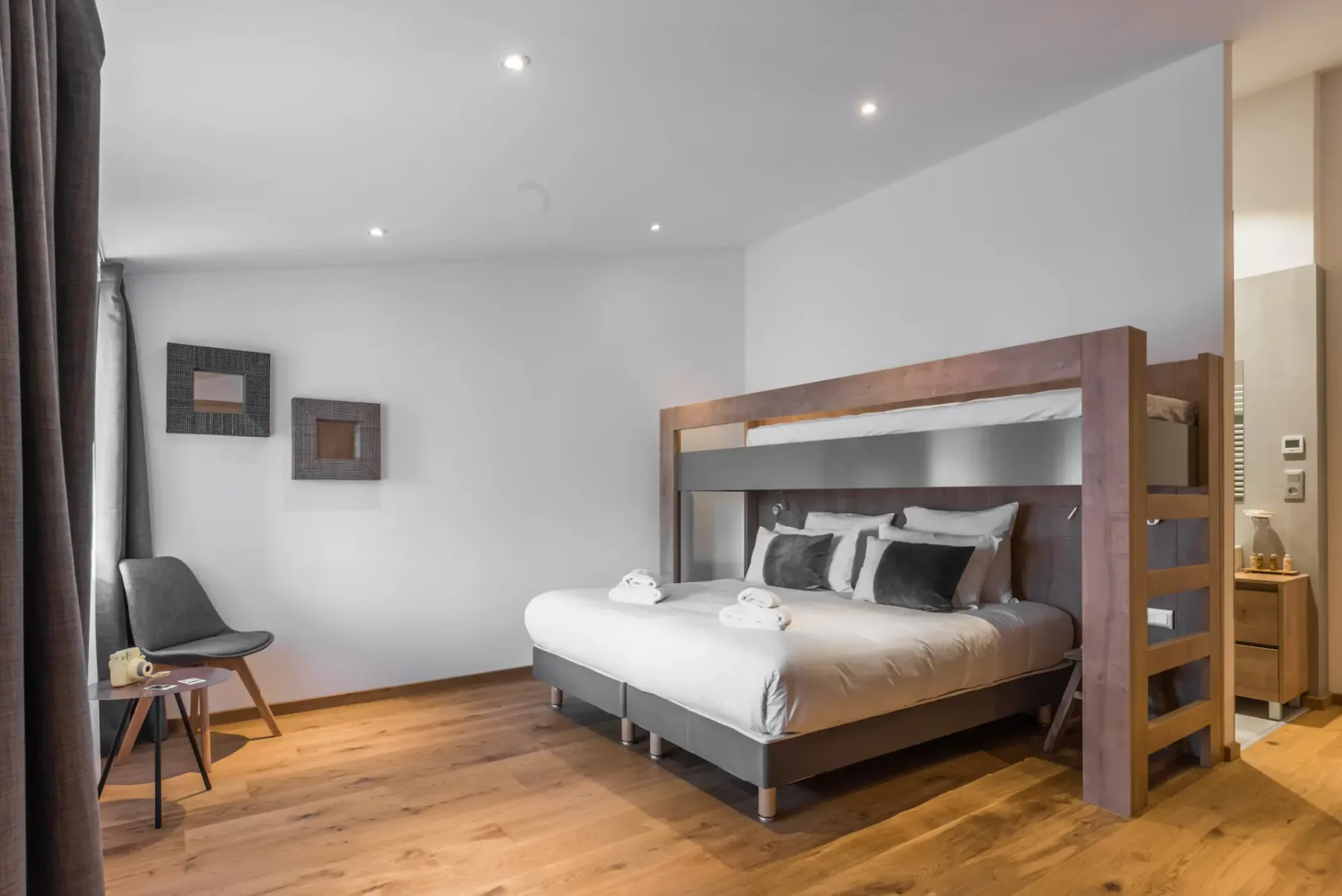 A bedroom with a large bed beneath a wooden loft frame and light wood flooring.