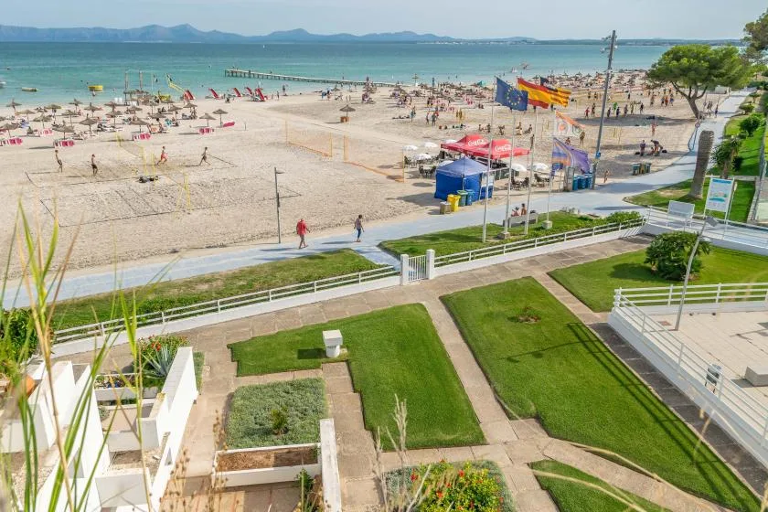 A landscaped lawn and walkway overlook a sandy beach and the sea.