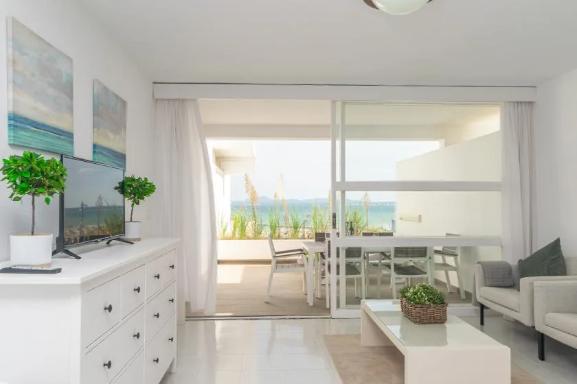 A bright living room opens onto a glass-enclosed balcony with a view of the water.