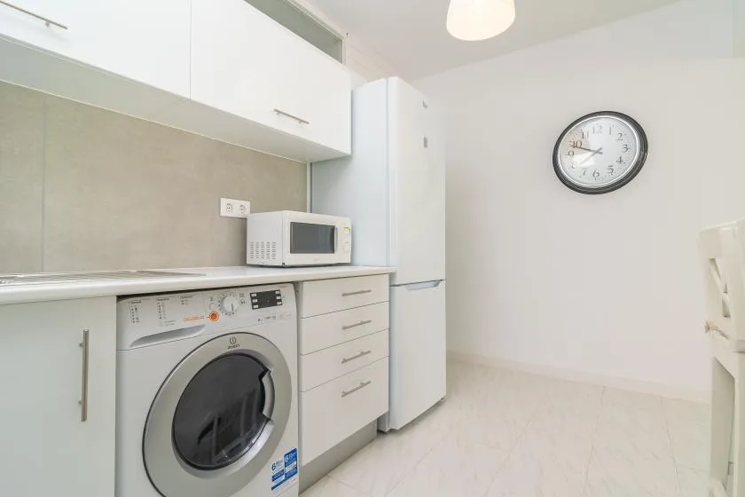 A bright kitchen with a washing machine, microwave, and refrigerator.