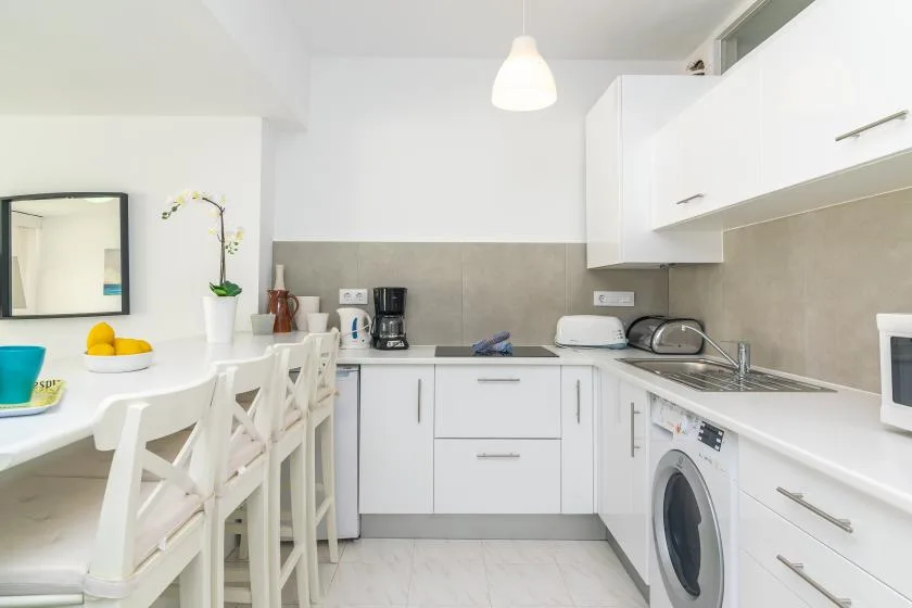 A bright white kitchen with a dining table, countertop appliances, and a washing machine.