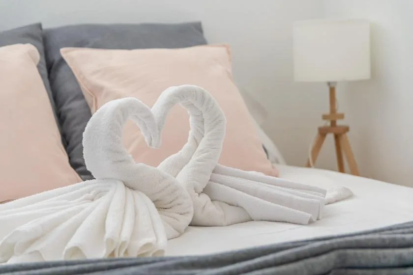 A bedroom with folded towels arranged in a heart shape on the bed.