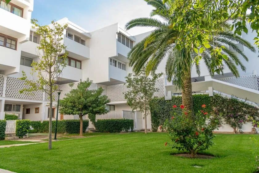 A landscaped courtyard with green lawn, trees, and a white multi-story building.