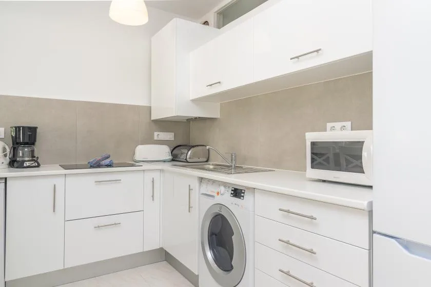 A bright kitchen with white cabinets, a washing machine, and countertop appliances.