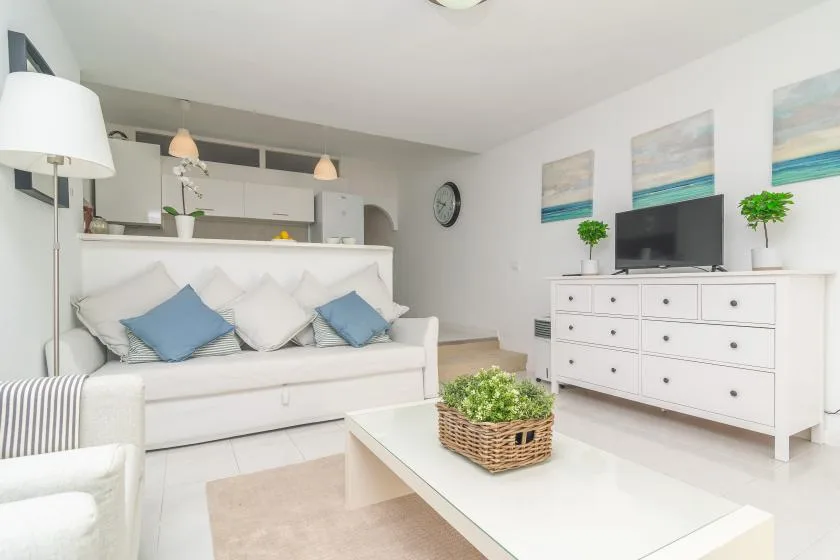 A bright living room with a white sofa, coffee table, and television.