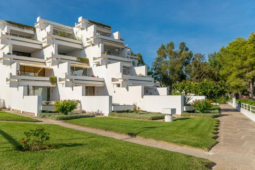 A white multi-level building beside a landscaped lawn and paved walkway.