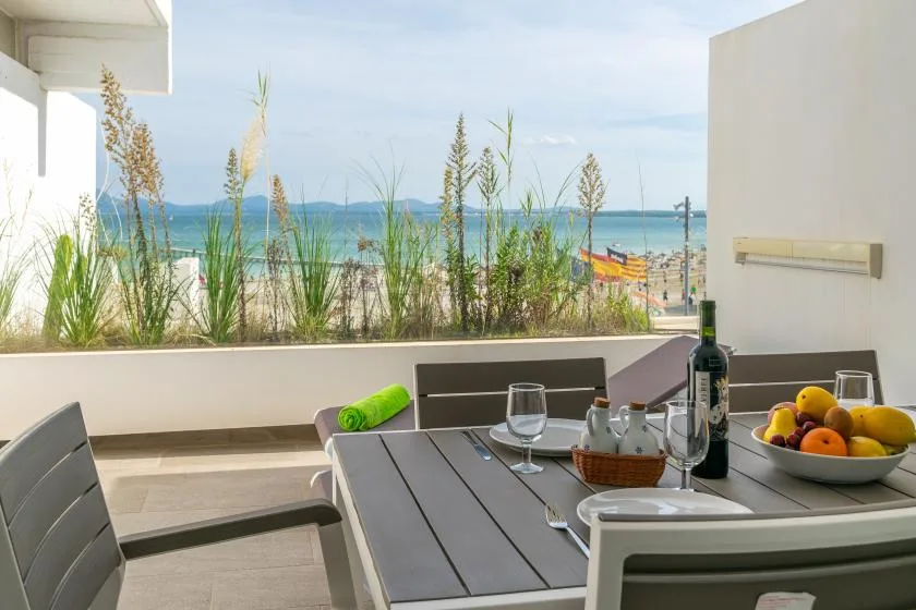 A seaside terrace with a dining table overlooking the beach and water.