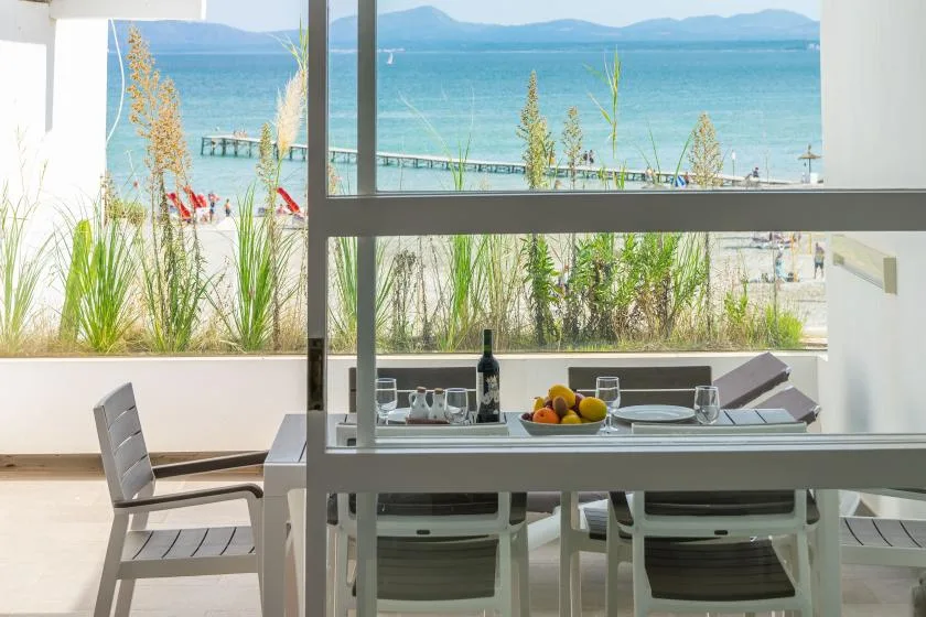 A dining table and chairs sit beside a large window overlooking the water.
