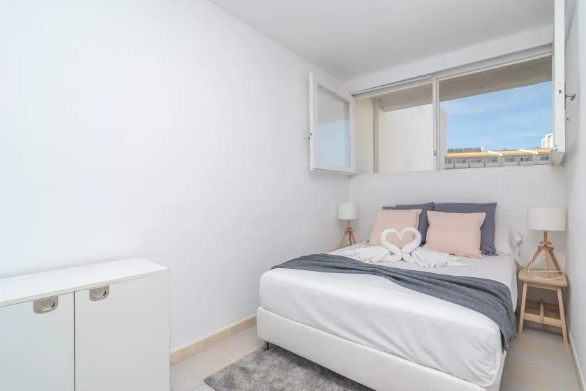 A bright bedroom with a bed, bedside tables, and an open window.