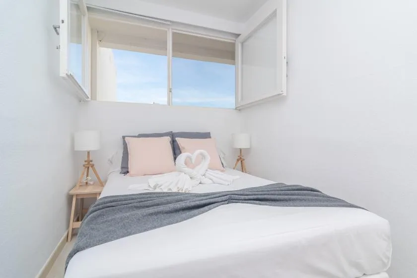 A bright bedroom with a neatly made bed beneath an open window.