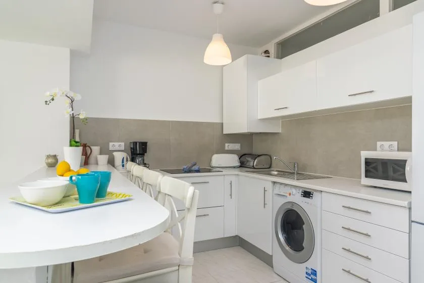 A bright kitchen with white cabinets, a dining table, and a washing machine.