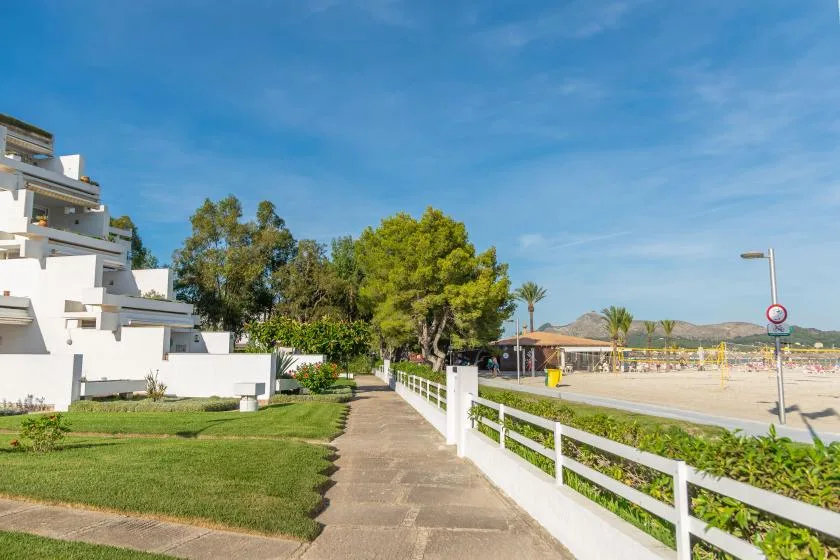 A paved walkway runs beside white buildings and a beachside fence under a blue sky.