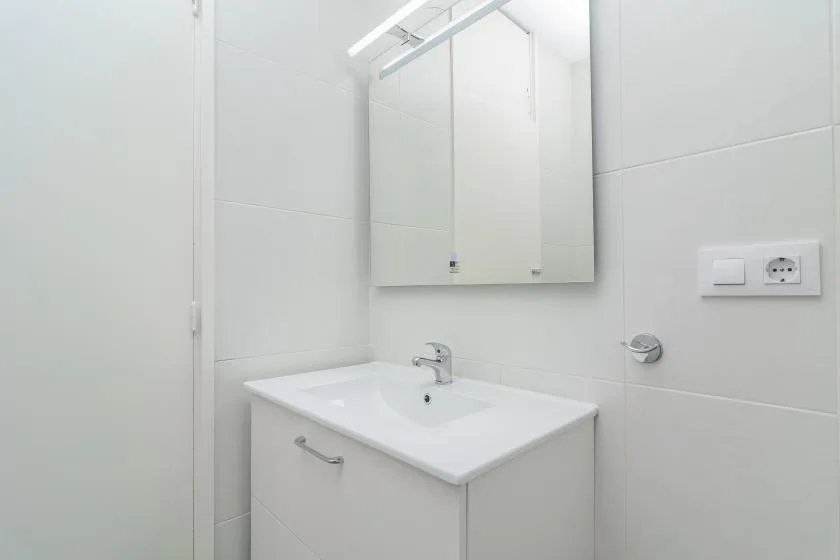 A bright bathroom with a white sink and mirrored cabinet.
