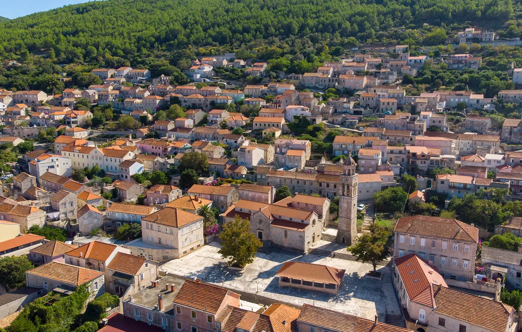 An aerial view of a hillside village with clustered buildings and surrounding greenery.