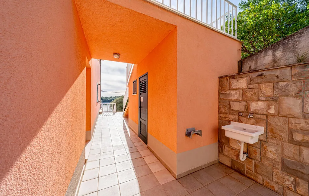 An orange exterior passage opens onto a tiled walkway beside a stone wall.
