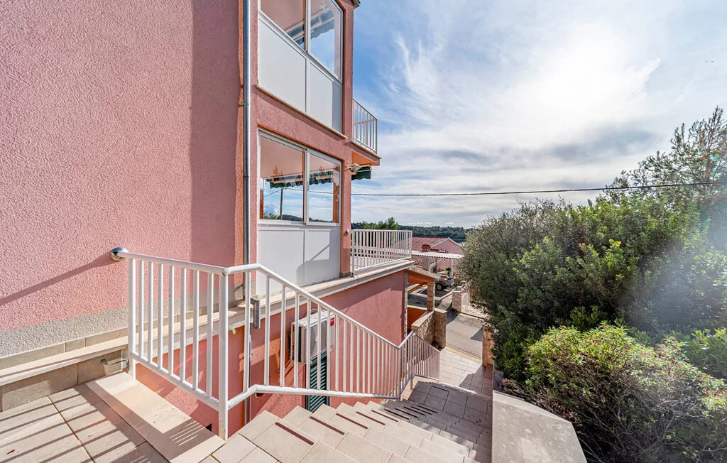 Exterior steps and a railing beside a pink building overlook a landscaped hillside.