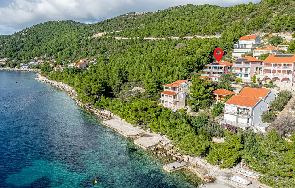 Aerial view of a coastal hillside with houses beside clear blue water.