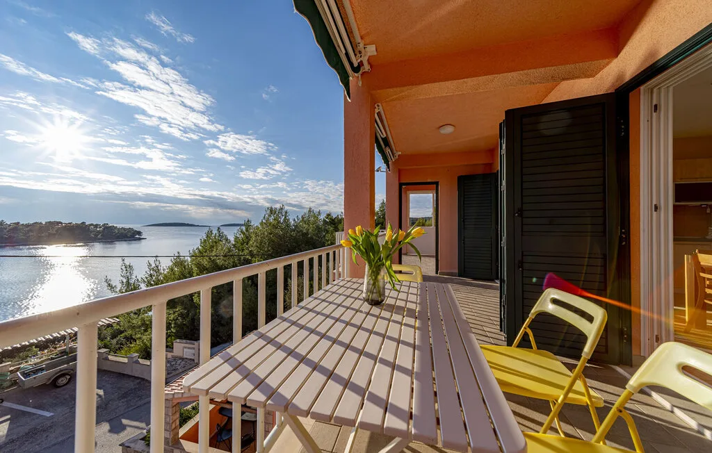 A balcony with outdoor seating overlooks the water and surrounding greenery.