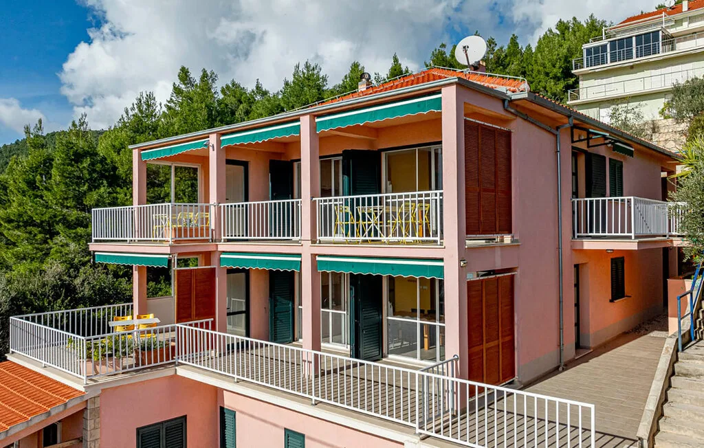 A pink multi-level building has balconies with white railings and green awnings.