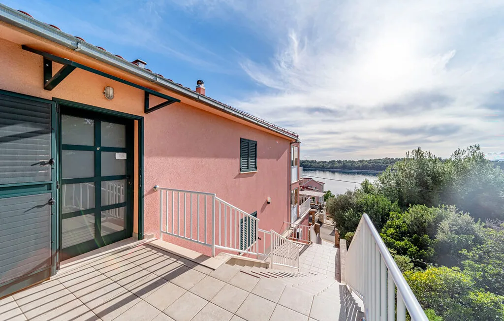 An outdoor tiled terrace beside a pink building overlooks trees and water.