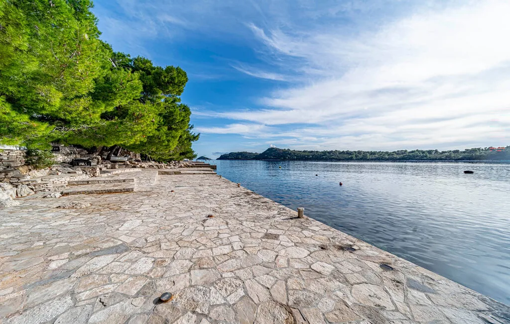 A stone waterfront promenade runs beside calm water and leafy trees.