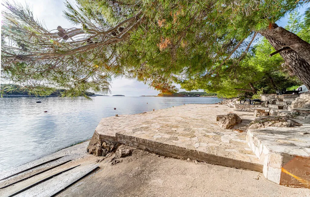 A stone terrace beside calm water, shaded by overhanging trees.