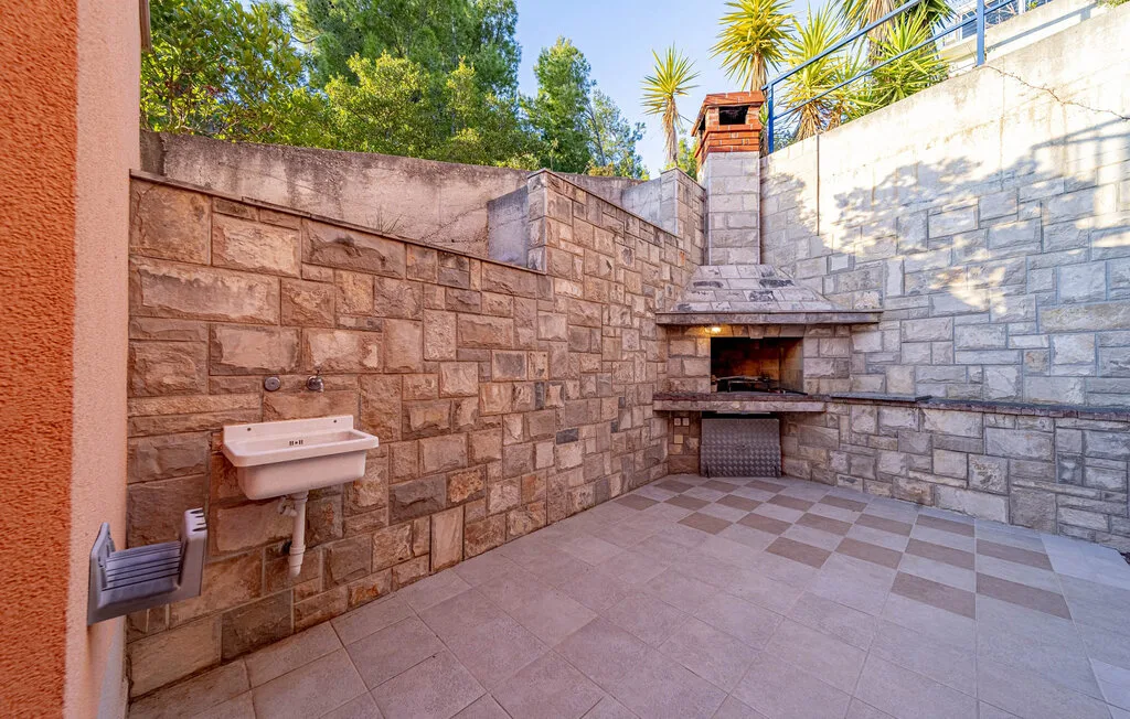 A stone-paved outdoor patio with a built-in barbecue and wall-mounted sink.