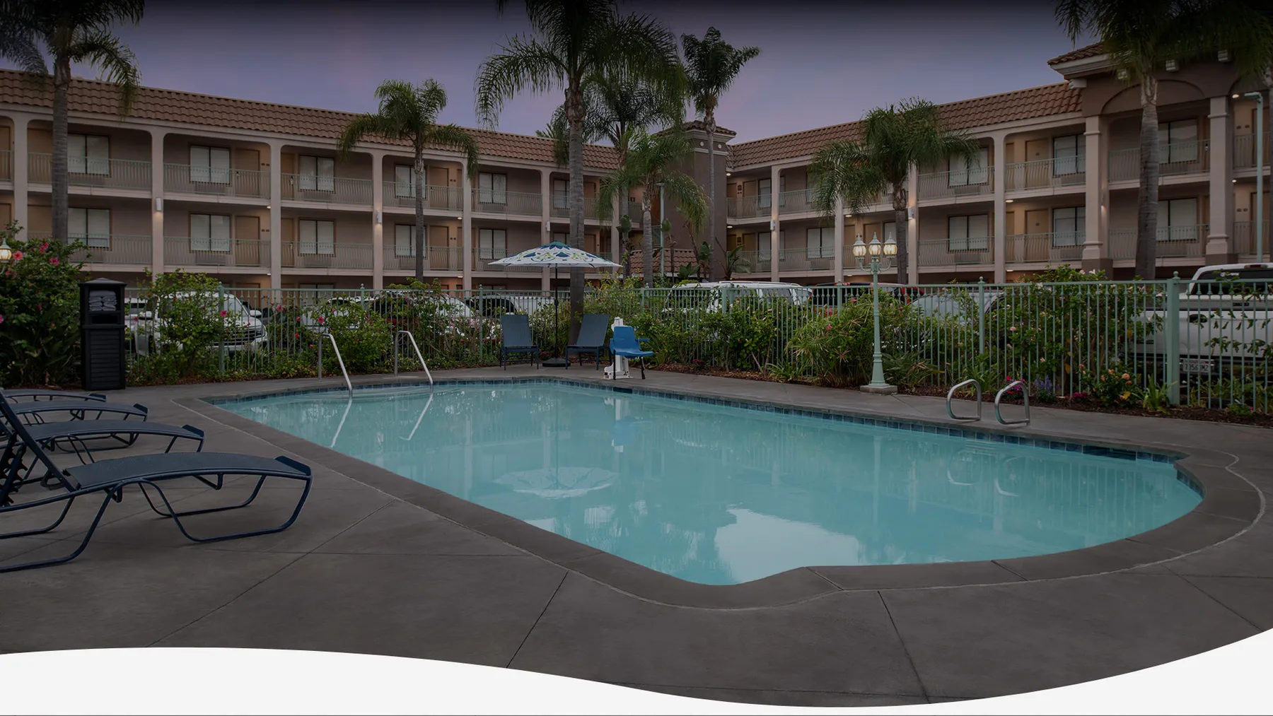 Piscina al aire libre con asientos y una valla junto al hotel