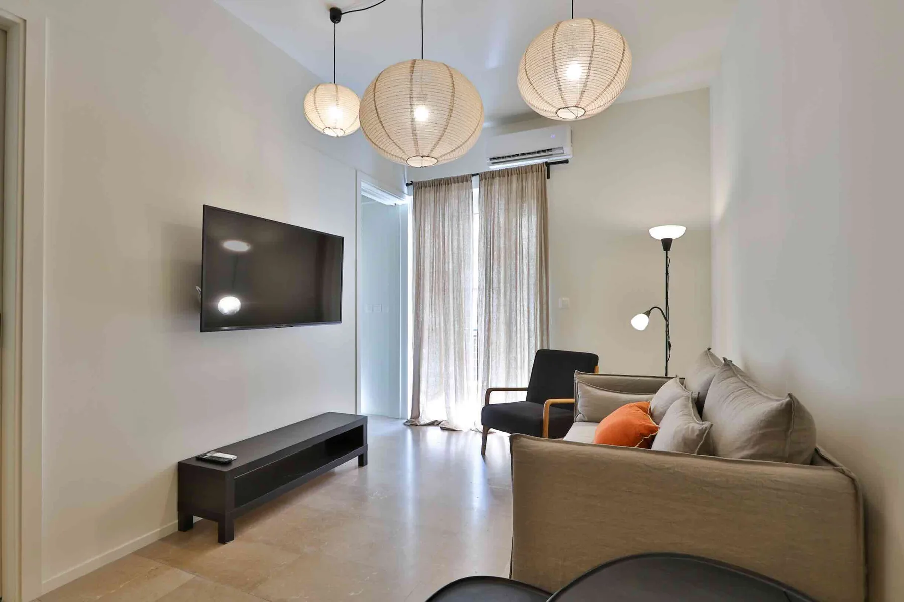 Una sala de estar con asientos, un televisor y ventanas altas con cortinas.