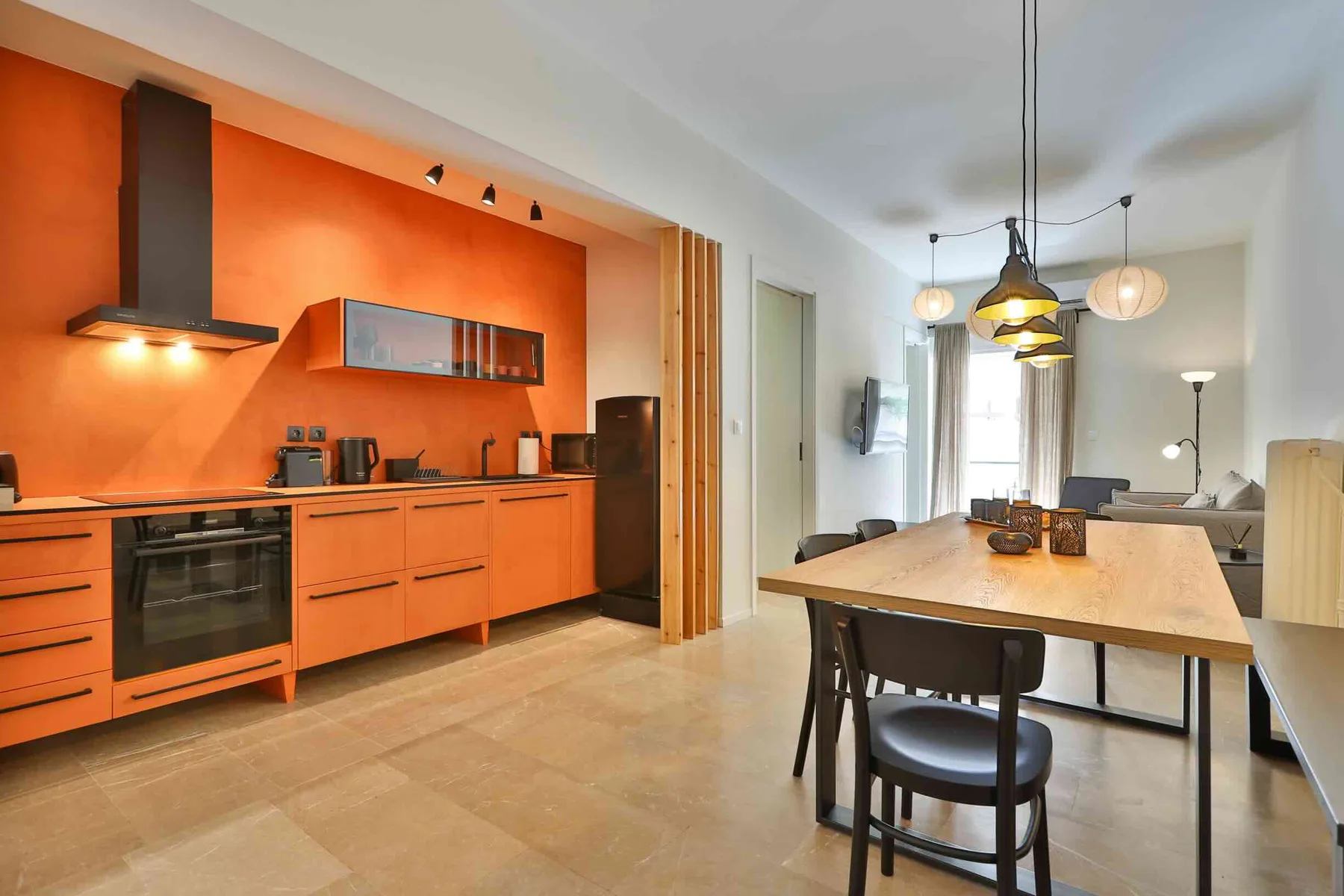 Cocina y comedor de concepto abierto con gabinetes naranjas y una mesa de madera.