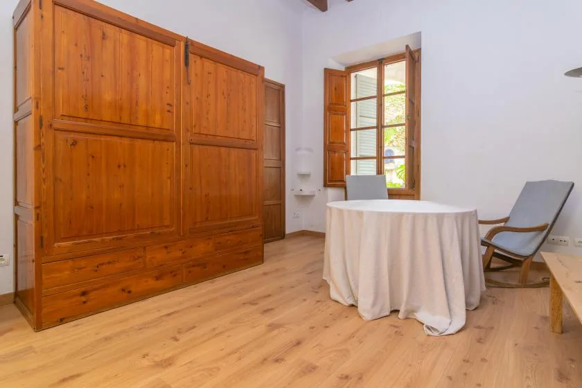 A bright room with a round table, seating, and a wooden shuttered window.