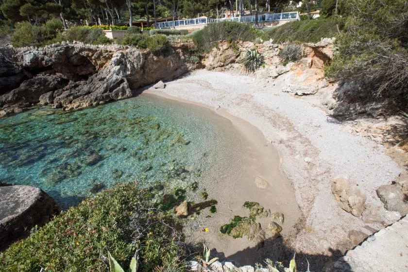 A small rocky cove with clear turquoise water and a sandy beach.