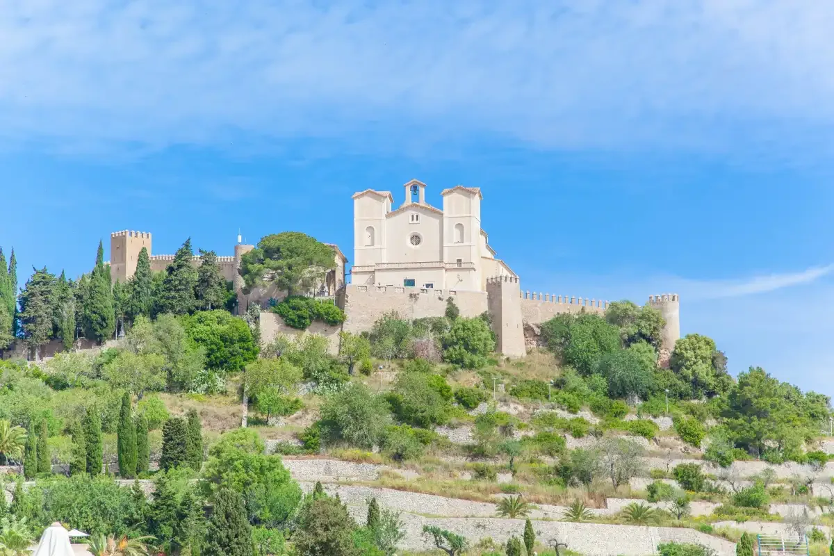 A hilltop church and stone fortifications rise above a green landscape.