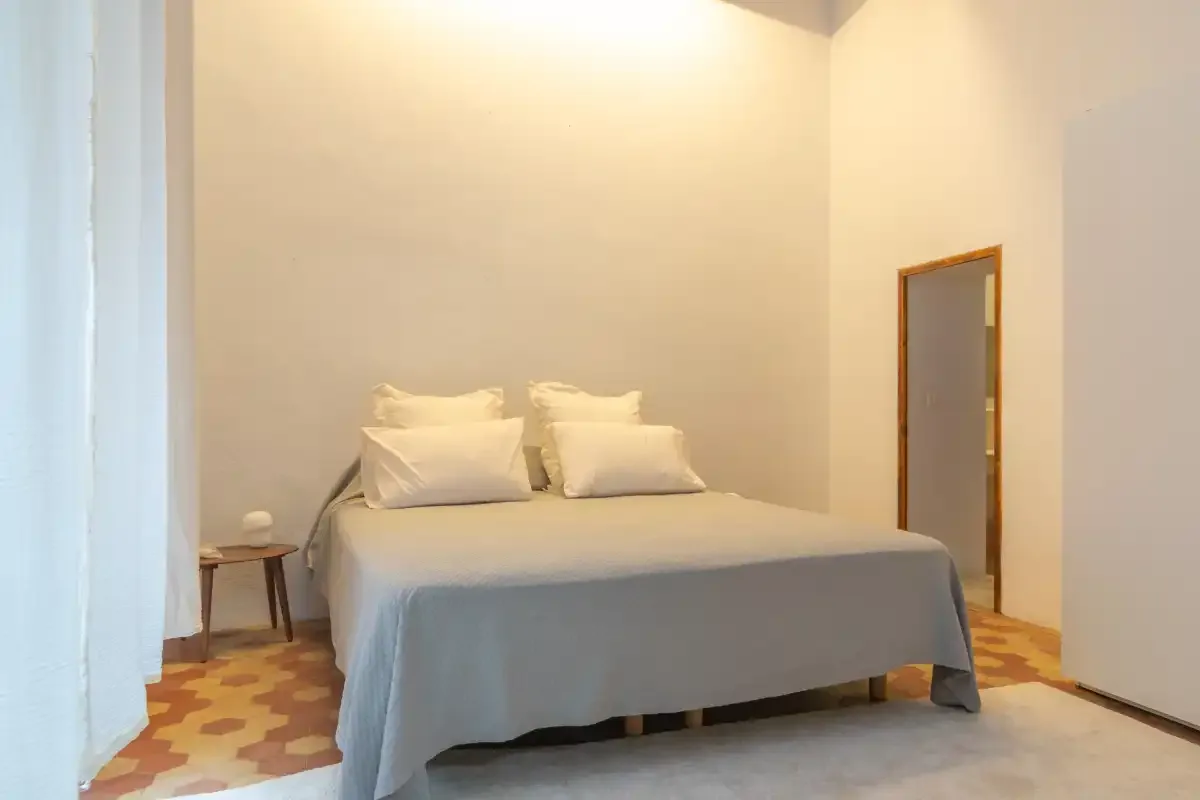 A bedroom with a bed covered in gray bedding and a small bedside table.