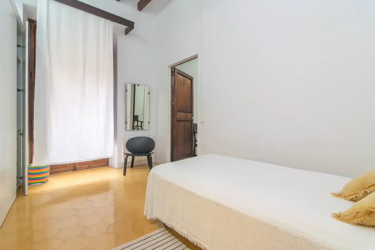 A bedroom with a bed, a curtained window, and a small chair.