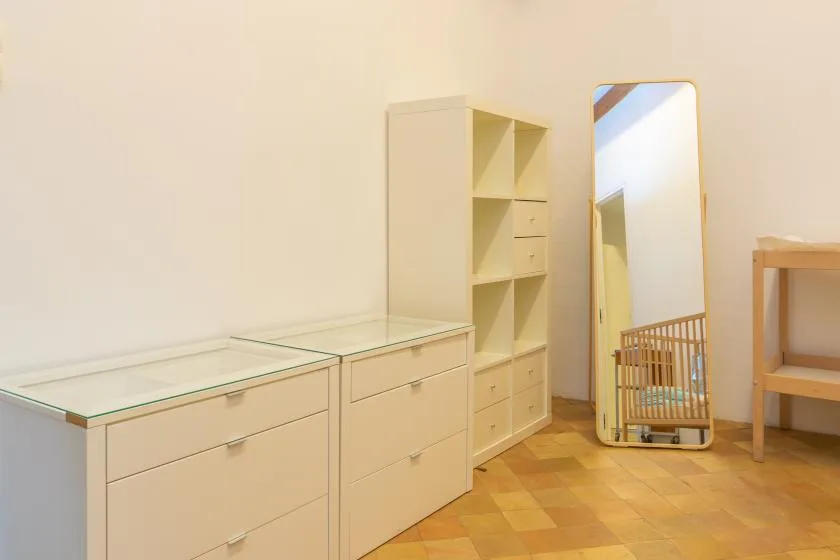 A bright room with low storage cabinets, open shelving, and a full-length mirror.