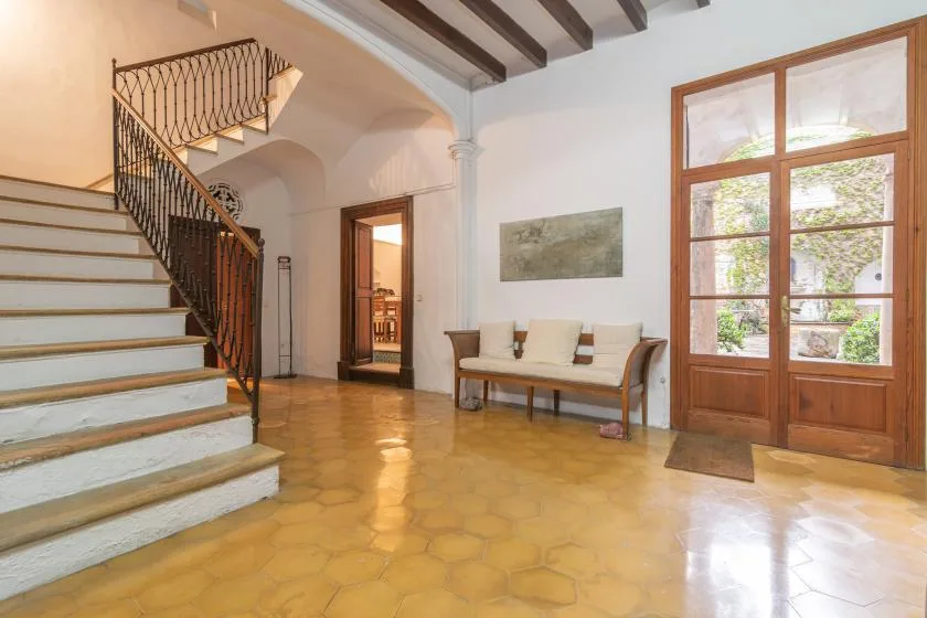 A bright interior hall features a staircase, a bench, and wooden-framed glass doors.