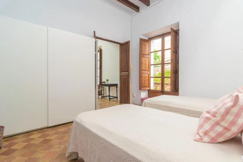 A bright bedroom with two beds and an open wooden window.
