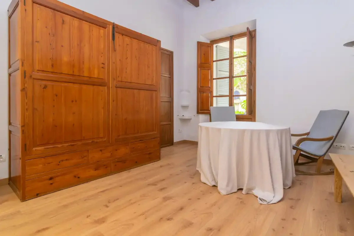 A bright room has a round table, wooden storage, and an open window.