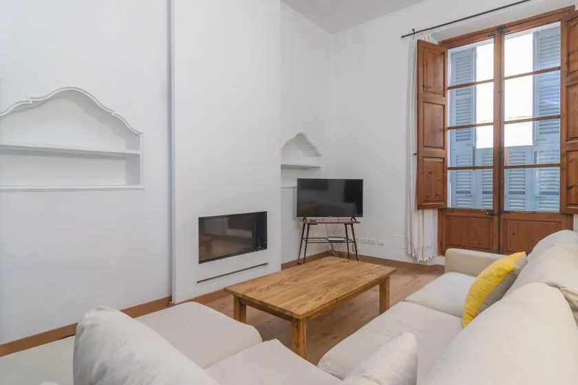 A bright living room with seating, a wooden coffee table, and a large window.