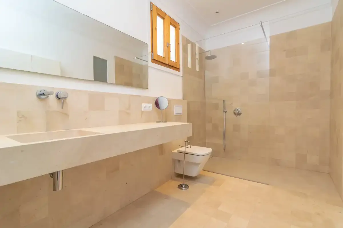 A tiled bathroom with a long sink counter, mirror, and shower.