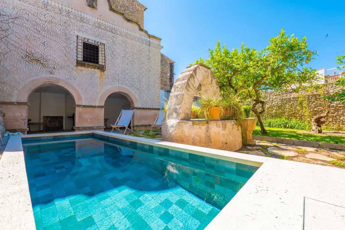 A courtyard pool sits beside a stone arch and leafy tree.