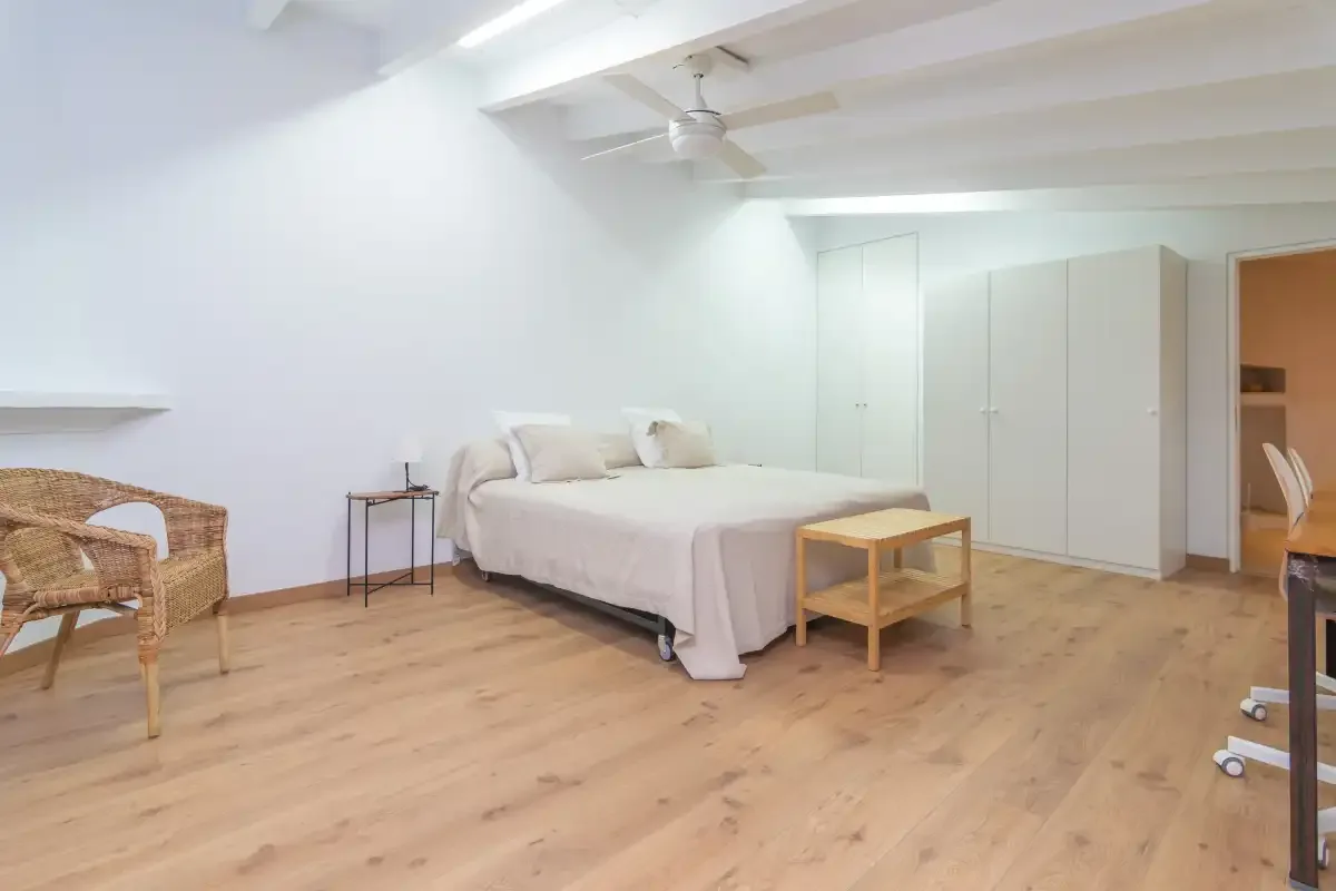 A bright bedroom with a bed, light wood flooring, and a ceiling fan.
