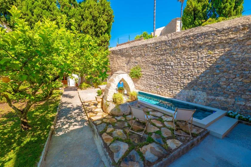 A stone courtyard features a small pool beside a high stone wall.